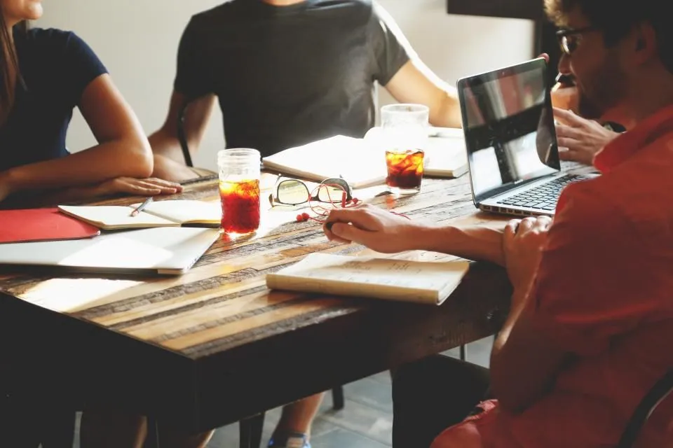Personas trabajando juntas con laptops y libretas